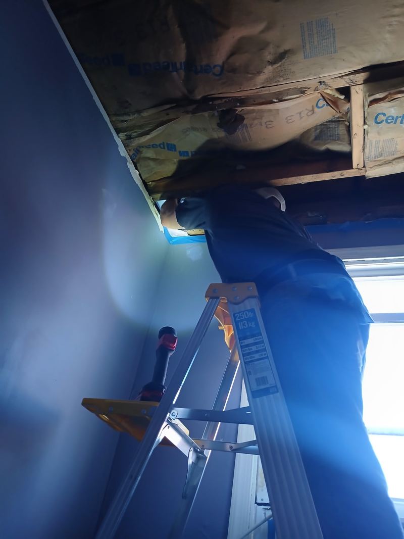 Inspecting an opened ceiling cavity by flashlight from a step ladder
