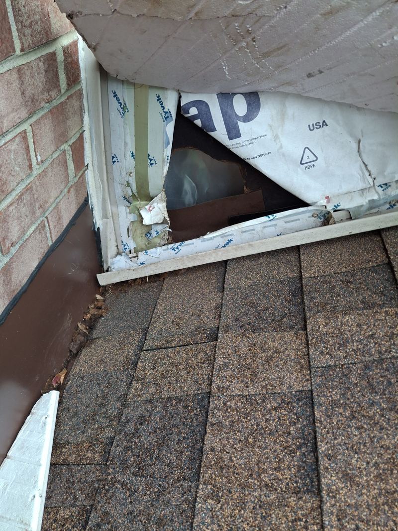 A torn opening in house wrap beneath a soffit corner, exposing the wall cavity